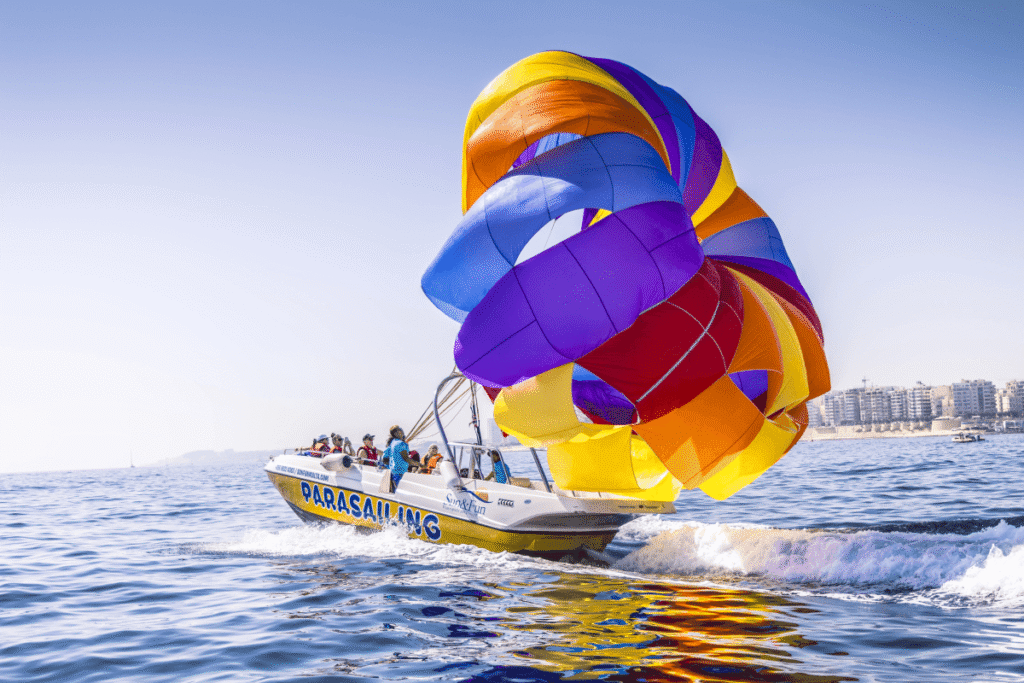 Dos personas practicando parasailing sobre el mar con vistas a la costa de Malta