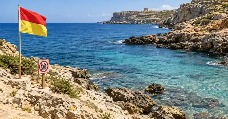 Bandera de seguridad junto a una cala rocosa de Malta.